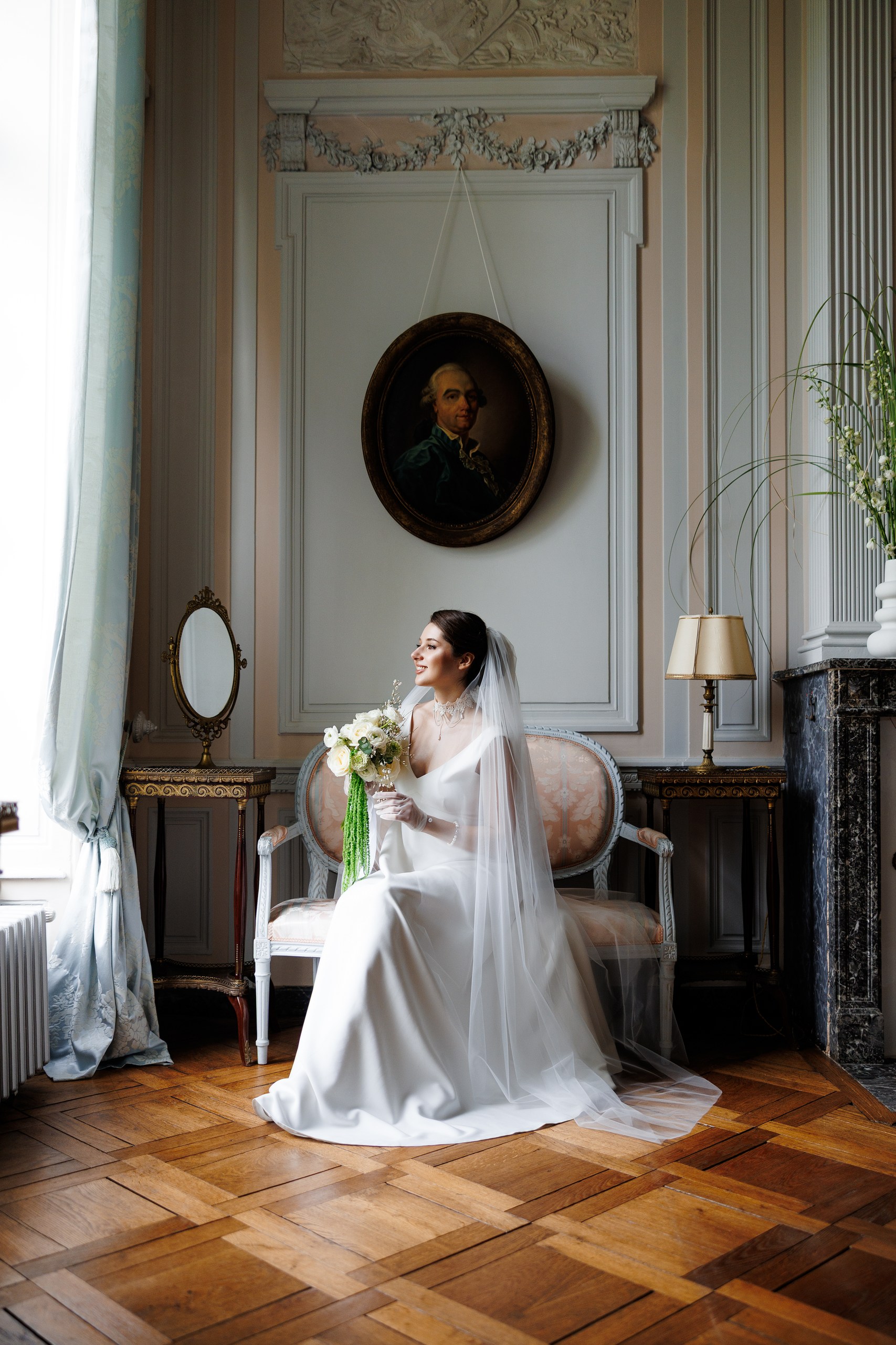 The bride seated in a period drawing room at Château de Bonnemare, holding her bouquet