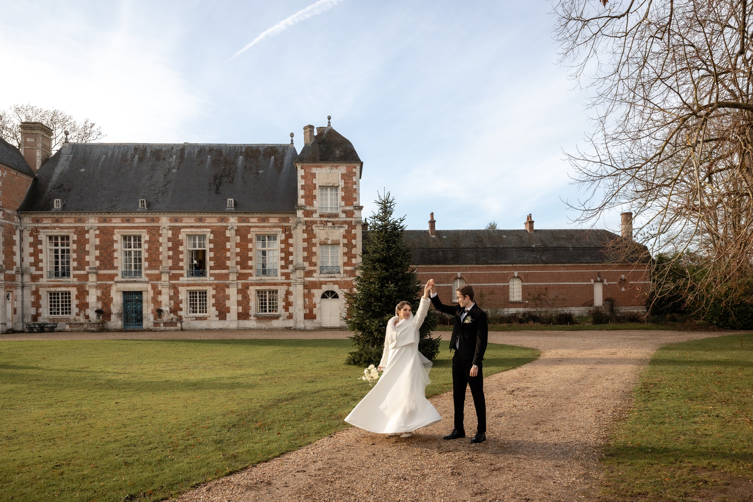 Newlyweds dancing hand-in-hand on the lawn in front of Château de Bonnemare