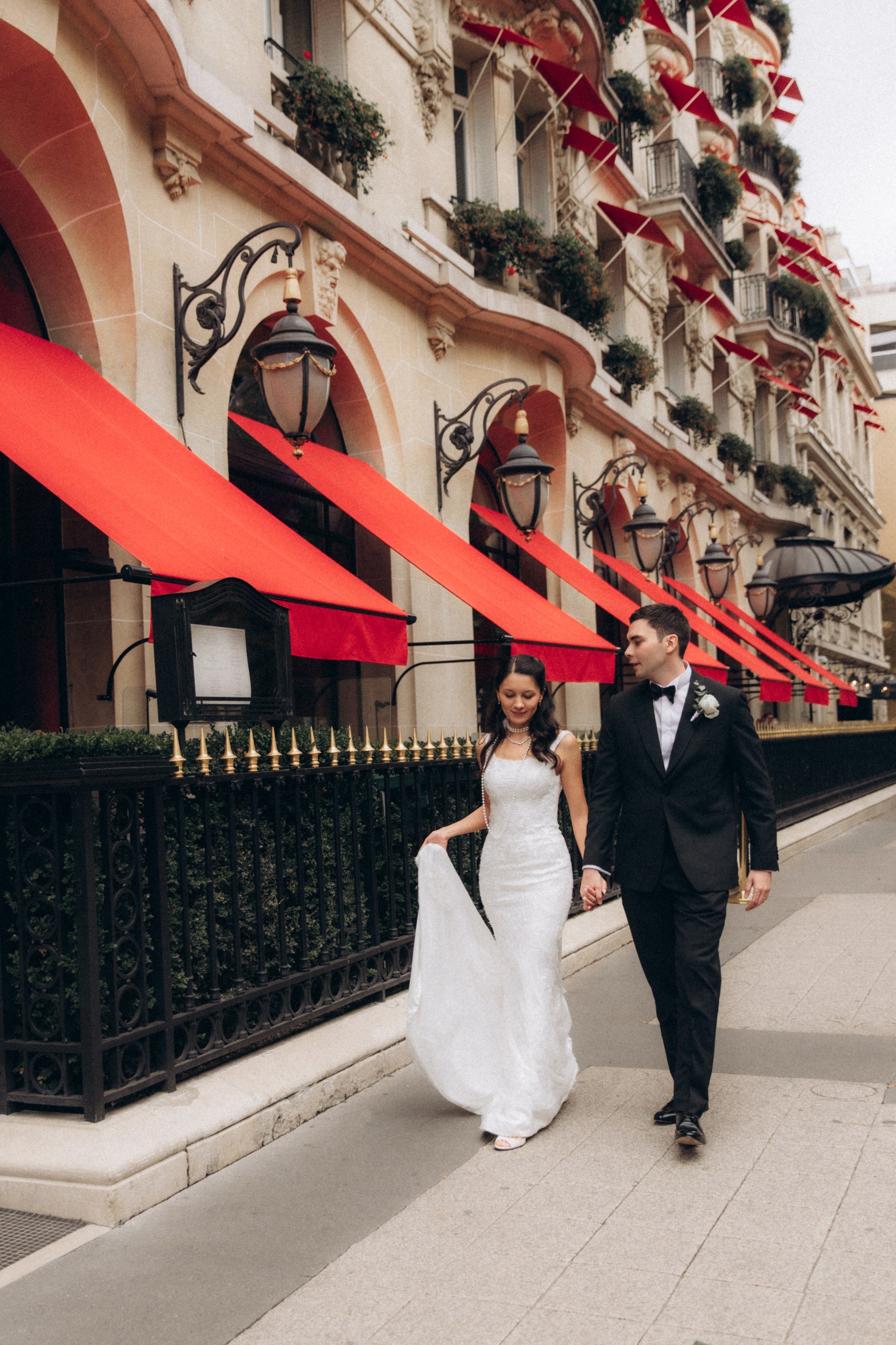 Jasmine and Ramil walking hand in hand past a Parisian hotel façade